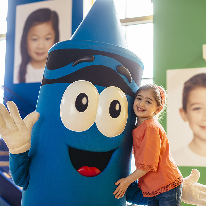 Young girl posing with giant costumed crayon