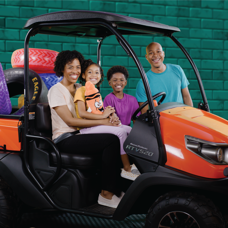 Family smiling sitting in an RTV with colorful tires in the back